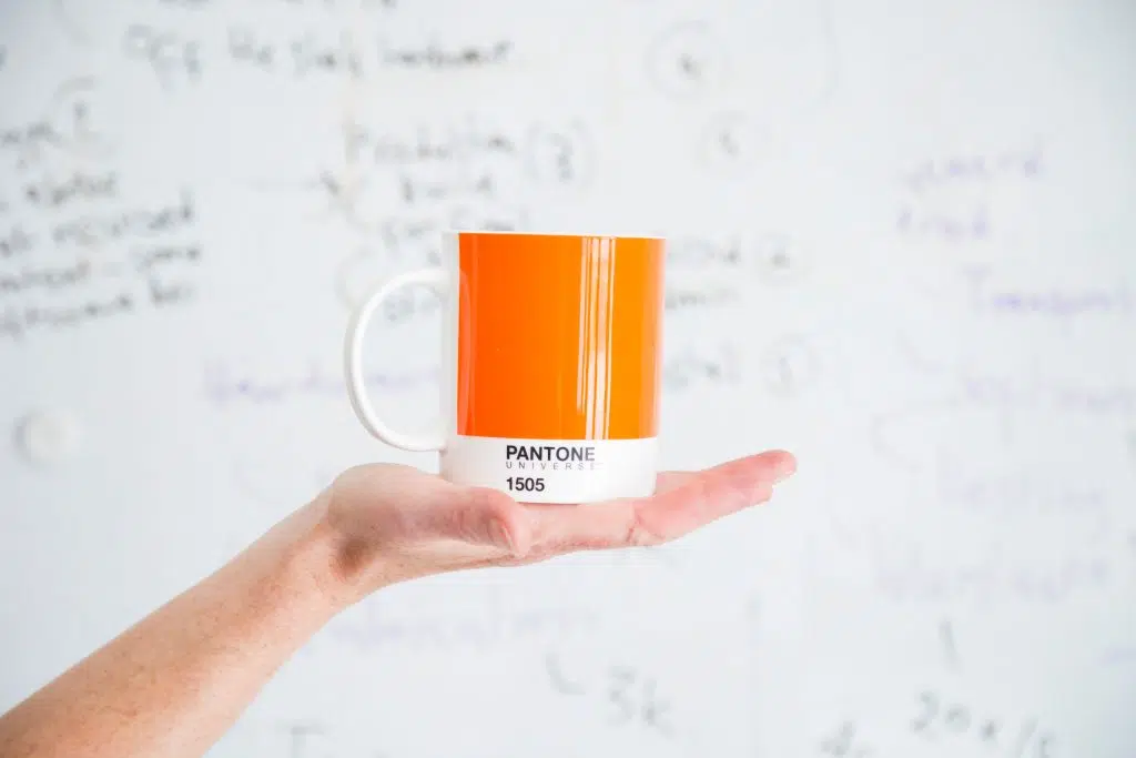 Open hand holding an orange Pantone coffee cup